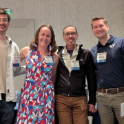 From left to Right - Four smiling adults linking arms in front of a podium