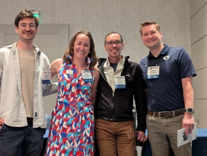 From left to Right - Four smiling adults linking arms in front of a podium
